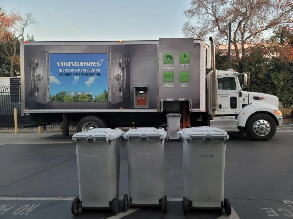 A garbage truck stands in front of a building, prepared for garbage collection.