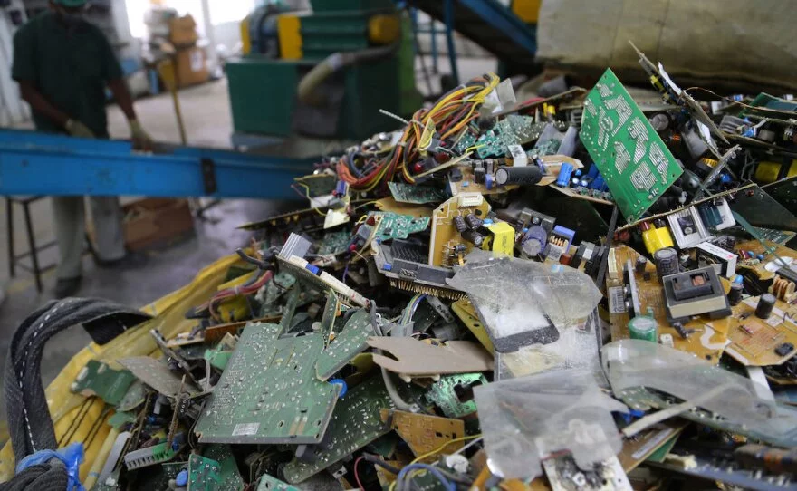 A man is diligently working with a variety of electronic parts piled up in front of him on a work surface.