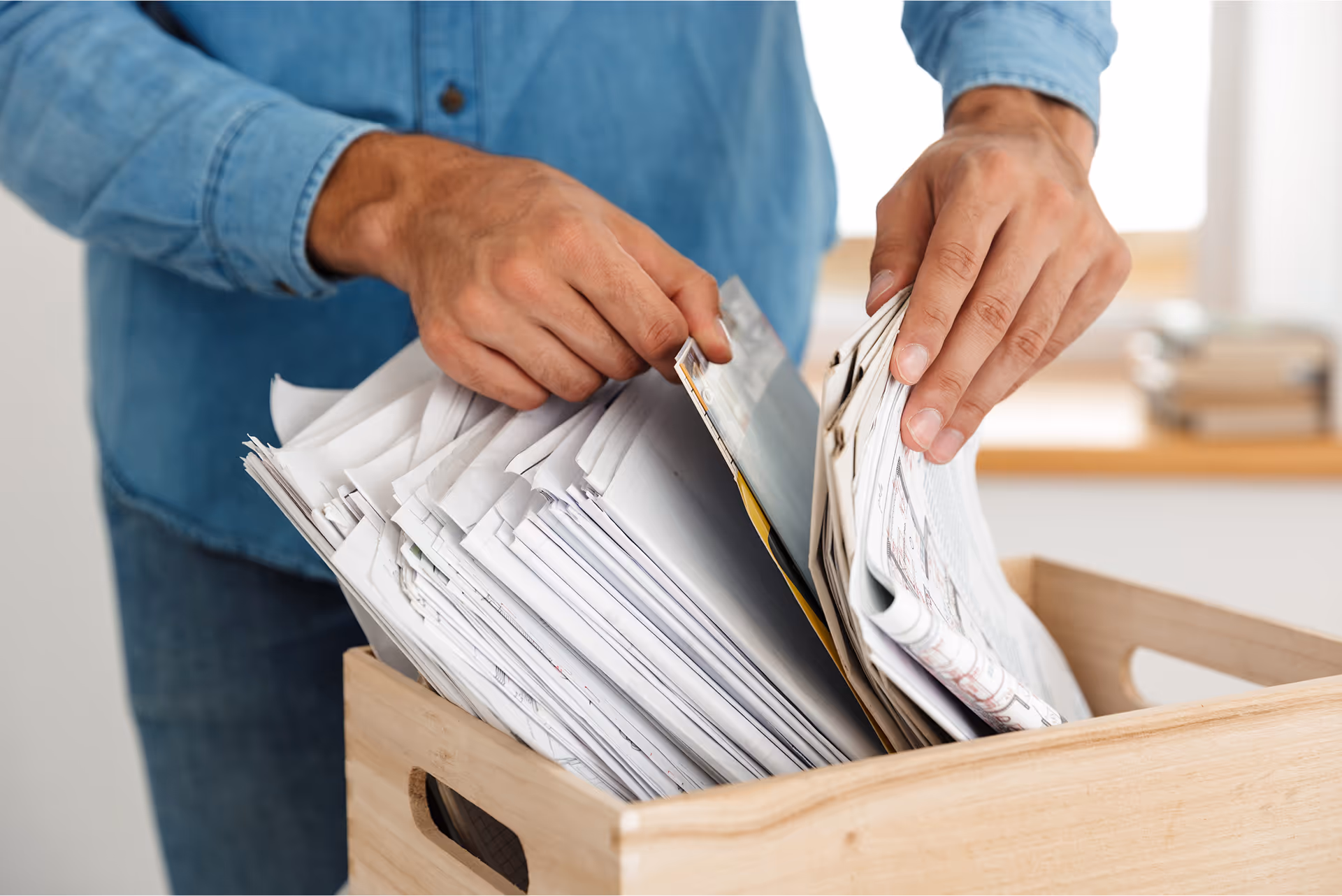 A person sorting a stack of paper documents and magazines inside a wooden crate.