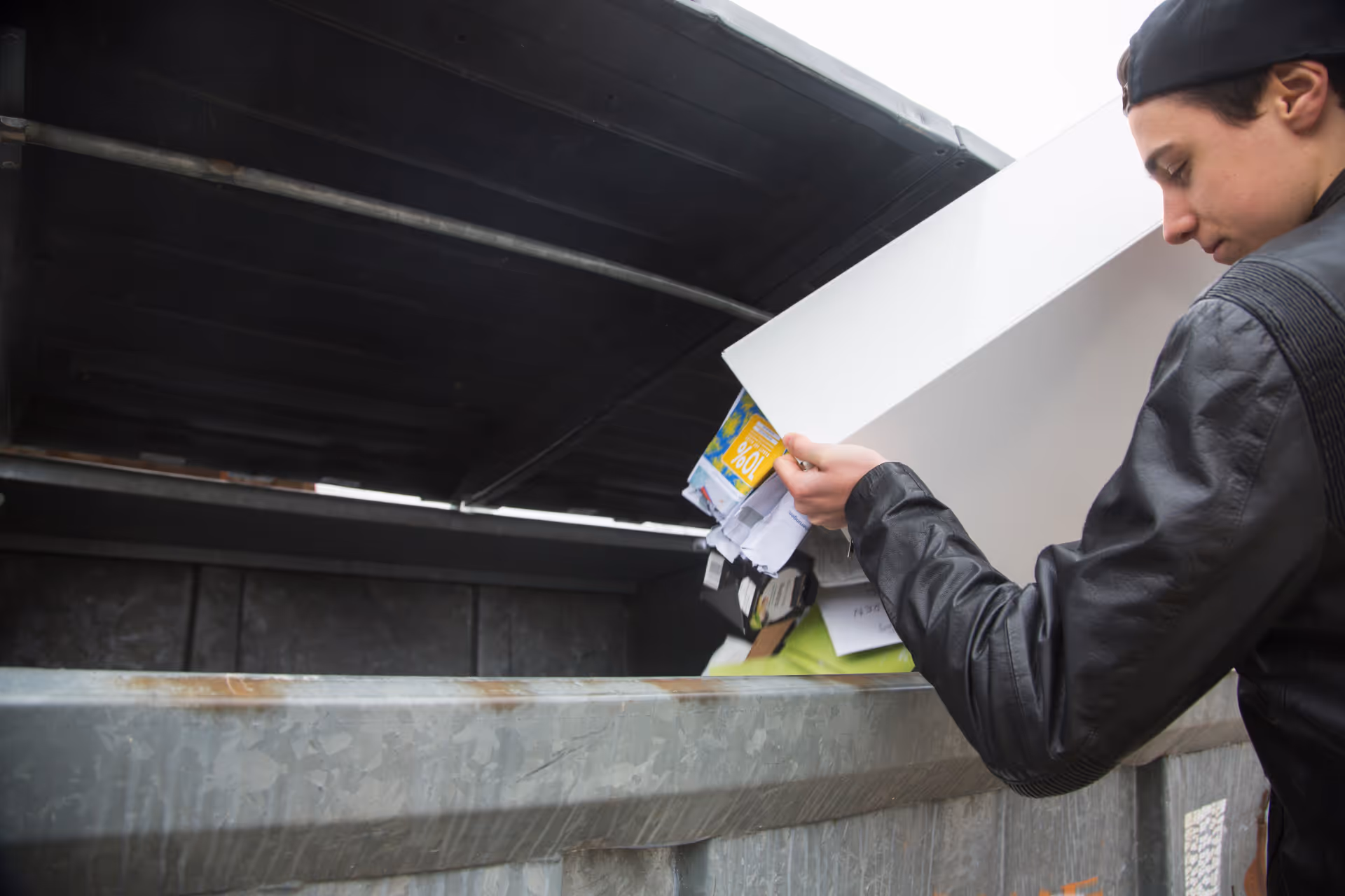 A worker emptying paper waste into a large recycling container.