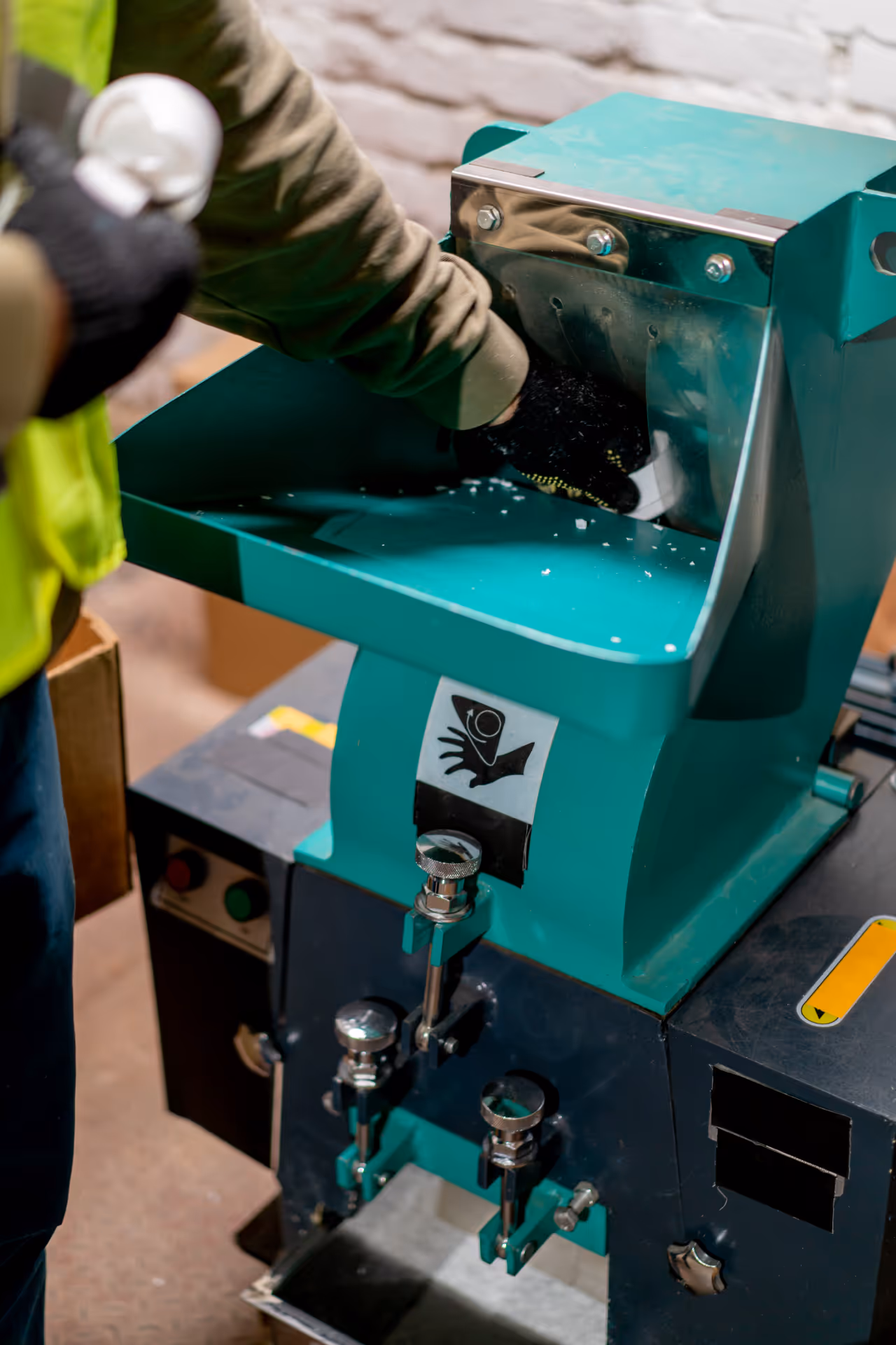 An industrial shredder being operated by a worker in safety gloves.