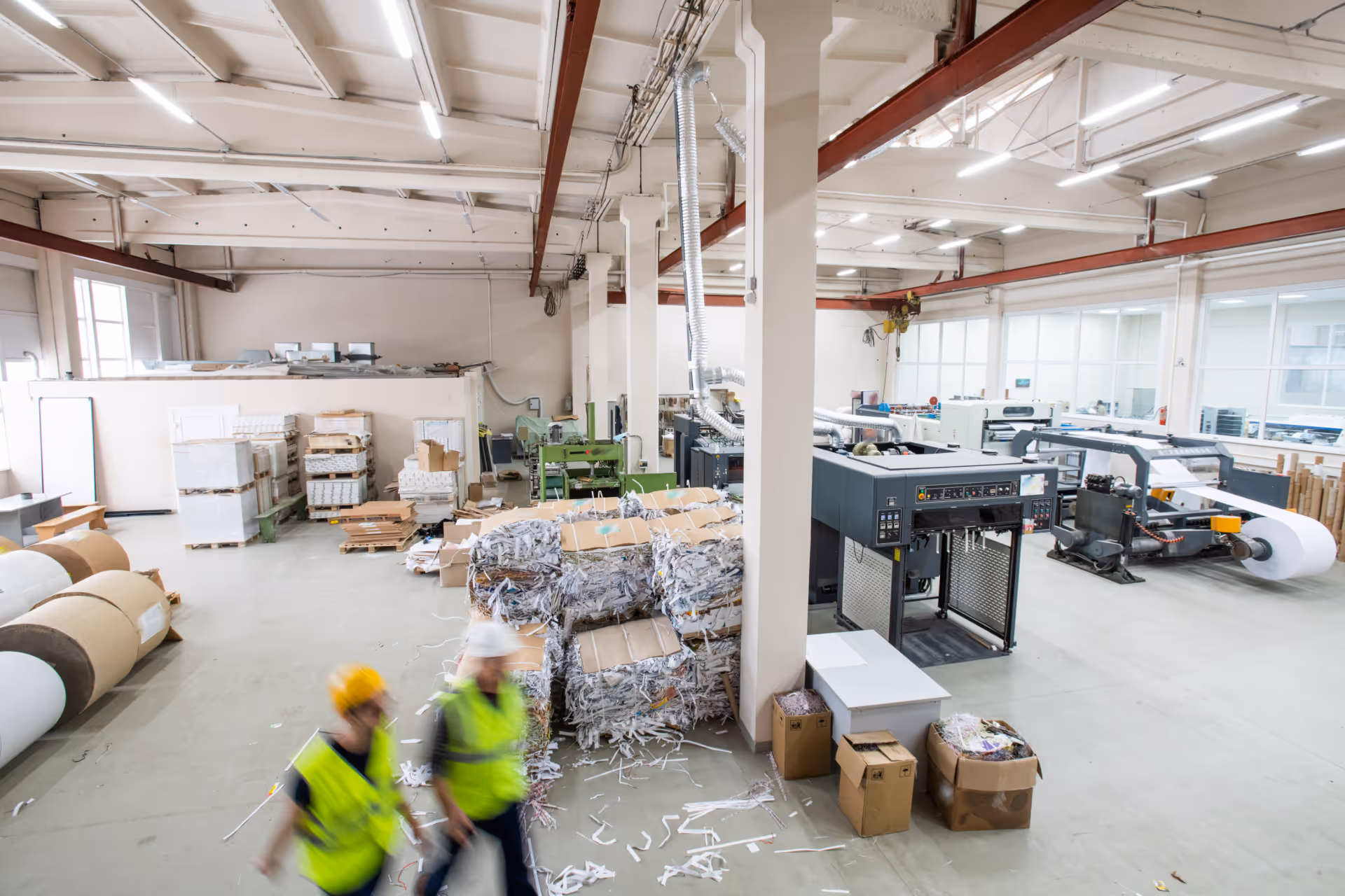 Industrial paper recycling facility with workers, paper rolls, and baled shredded paper.