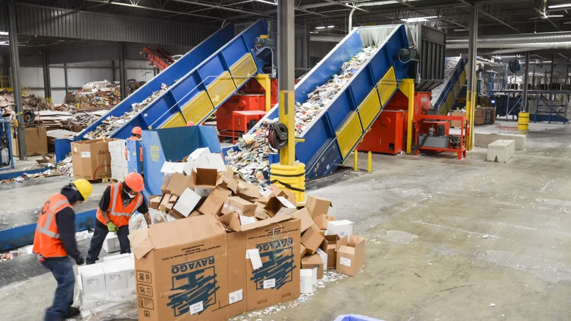 A team of workers loading boxes onto a conveyor belt in an industrial environment.