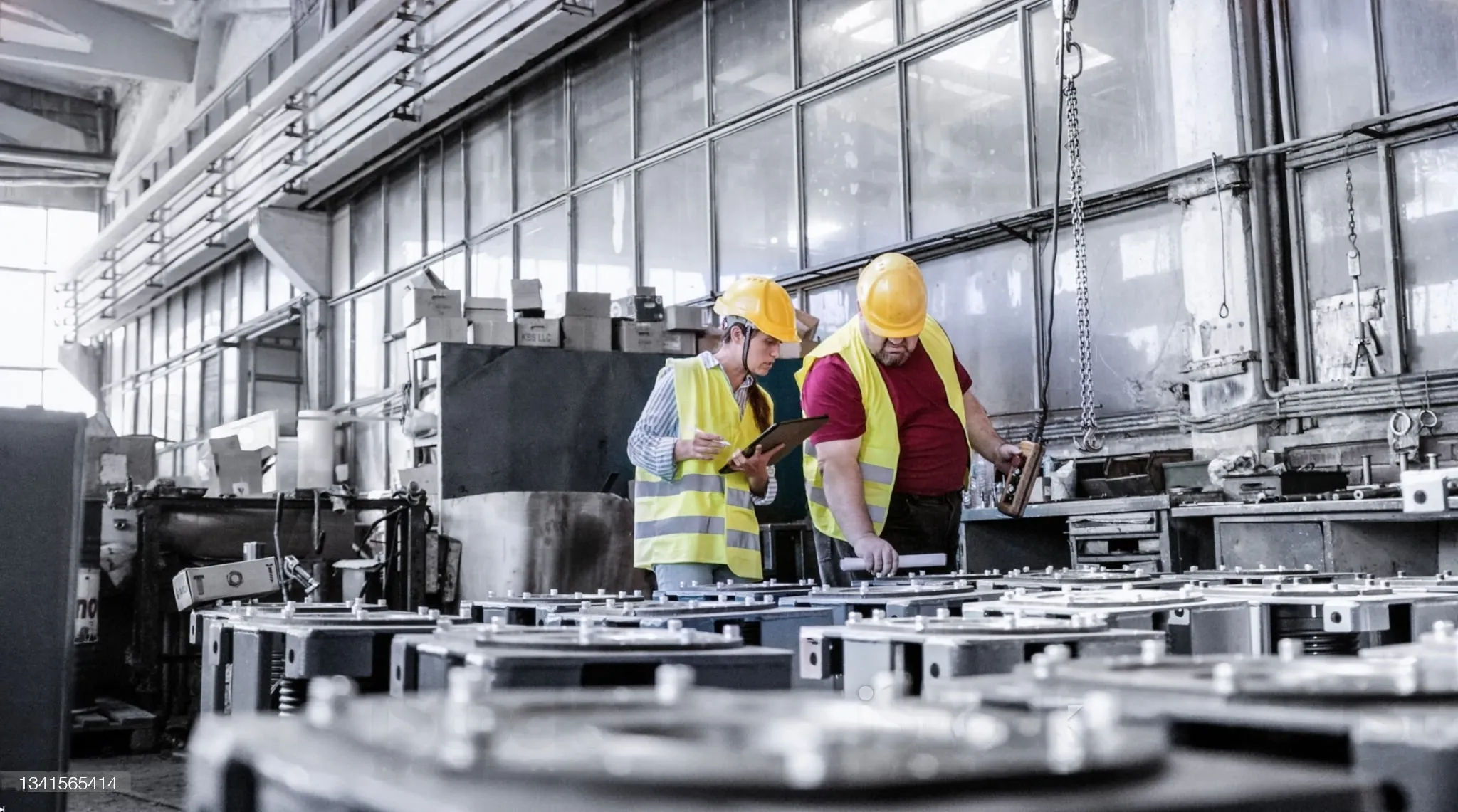 Two workers in a factory observing machinery, engaged in conversation about its efficiency.